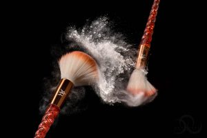 Product Photograph of two makeup brushes colliding, with a spray of powder